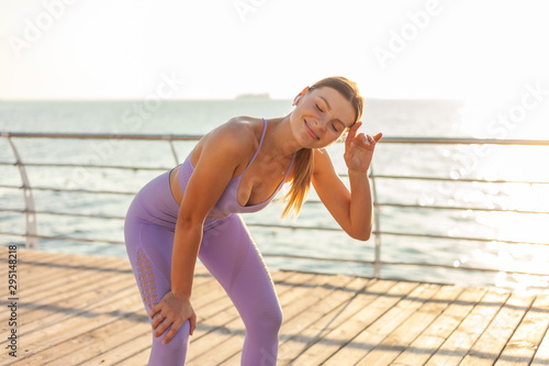 Morning running workout concept. Young tired fit woman in sportswear on the beach at sunrise.
