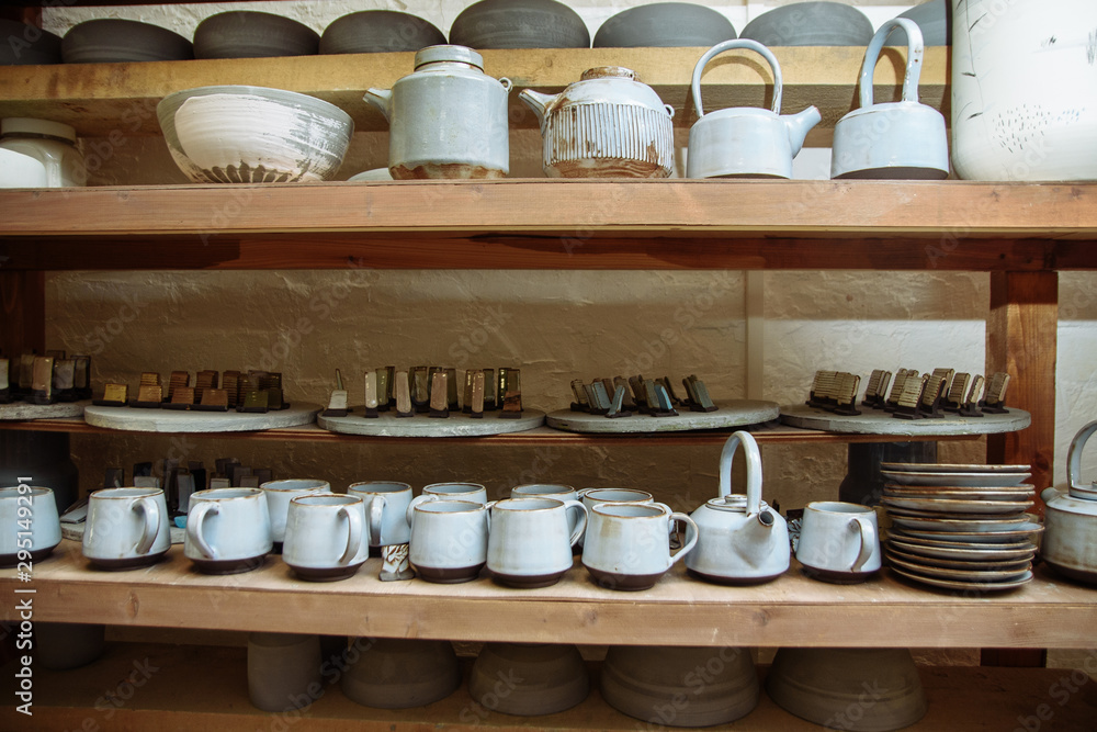 Handmade ceramic pottery in a potter's workshop. Clay plates, mugs and teapots on the shelves in the workshop studio