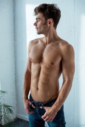 handsome shirtless man in blue denim jeans standing in bedroom