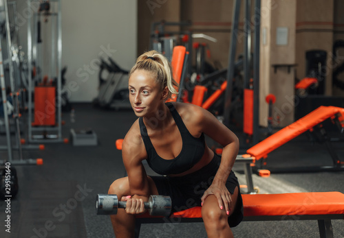 Young fitness woman doing concentrated doing dumbbell lifts for biceps one hand while sitting on a bench in the gym. Training concept with free weights.
