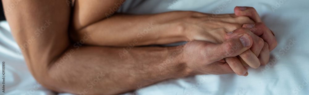 Fototapeta premium panoramic shot of passionate man and woman holding hands in bedroom