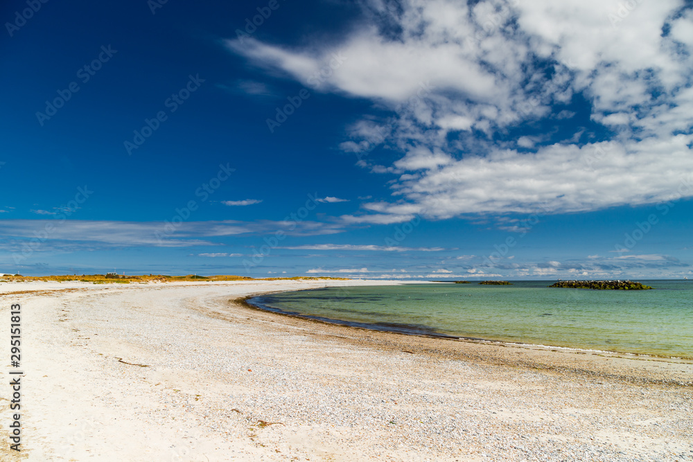 Fototapeta premium Küstenstrand mit grünem Wasser vor Horizont mit blauem Himmel und Wolken