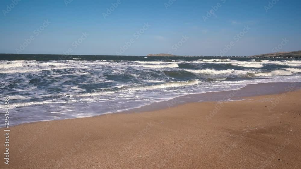Large storm surges on a deserted sandy beach against the backdrop of small mountains on a Sunny summer day. Large storm surges on a deserted sandy beach against the backdrop of small mountains on a Sunny summer day.