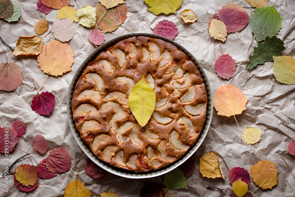 Fototapeta premium autumn browned fruit cake decorated with bright fallen leaves, top view