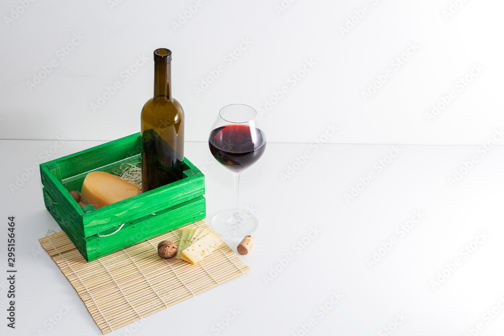 A bottle of red wine with a glass and a piece of cheese.