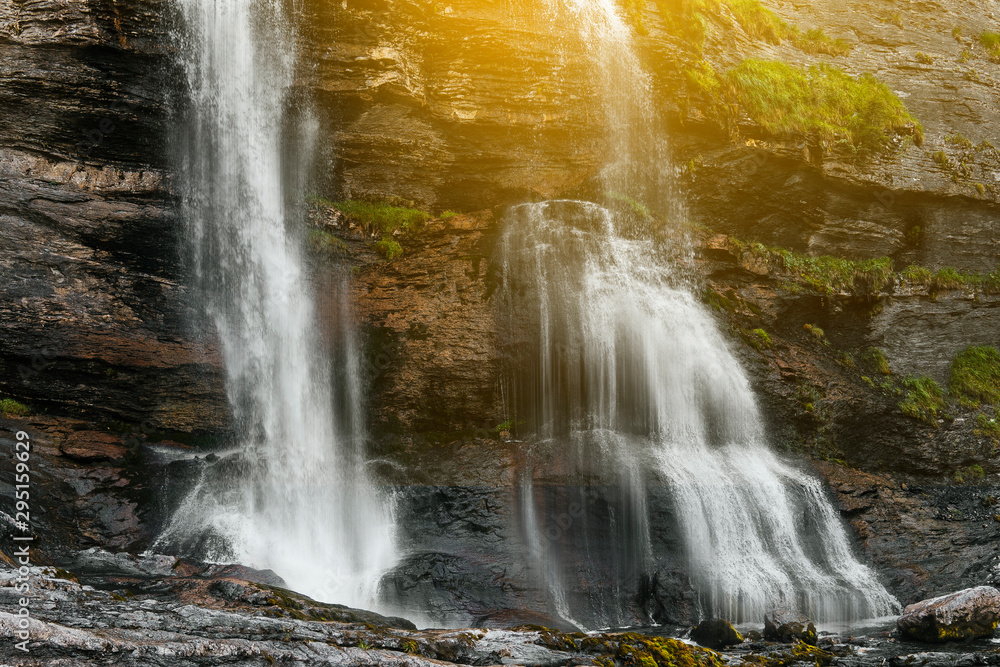 Obraz premium Alpine scenic mountain waterfall landscape covered with green glass, rocks. Sunny effect. Inspiring environment, outdoor activities, seclusion with nature. Travel and real life Concept. Wallpaper idea