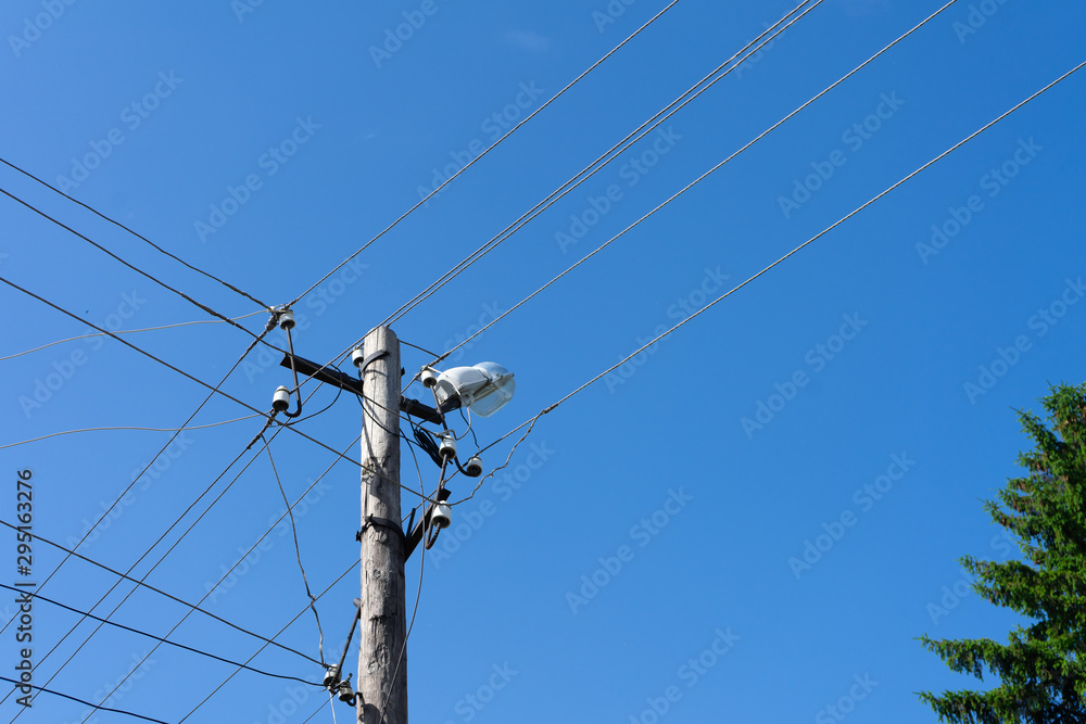 Old wooden electric pole with a lamp and many cables that run in different directions, cloud sky.