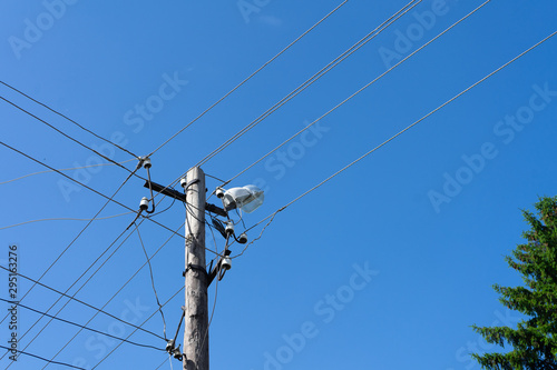 Old wooden electric pole with a lamp and many cables that run in different directions, cloud sky.