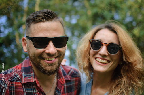 Close up portrait of young couple in sunglasses looking at the camera on green trees background, hipsters concept