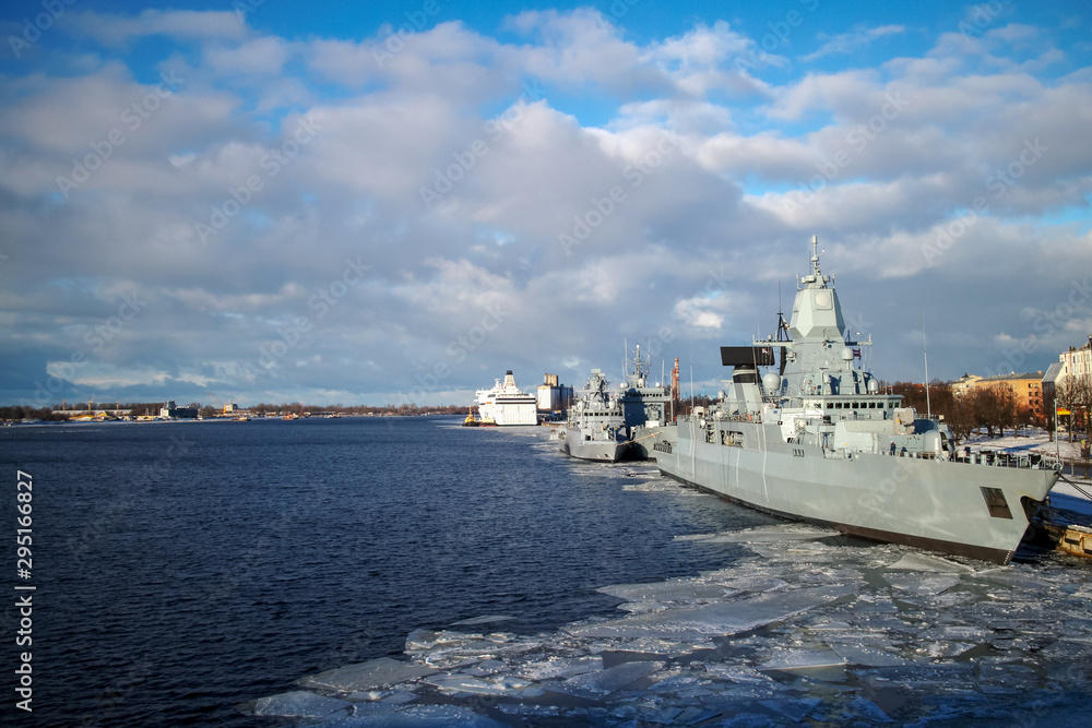 NATO warships in the city port in Riga, Daugava river landscape with blue sky and white clouds on the winter day and military grey vessel