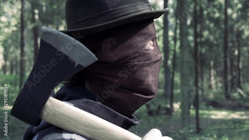 Serial maniac with axe in forest looking someone to kill. Bloody killer, murderer, mad man in   scary mask with beastly grin and crazy eyes. Halloween costume, horror concept.