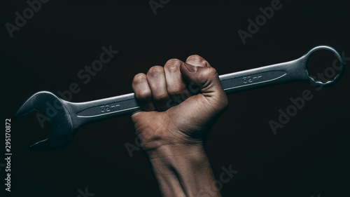Auto maintenance service. Strong male mechanic hand holding wrench over dark background.