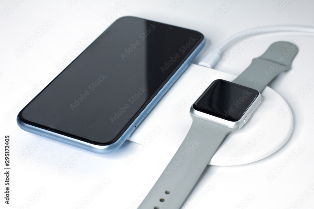 Cell mobile smartphone and smartwatch charging on a wireless charge. New devices, equipment. Modern technology concept. Still life, composition of gadgets: phone, watches, charger. Easy way to charge.