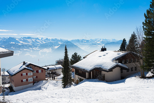 Majestic unique misty blue alpine skyline aerial panorama of Rigi resort. Snow-capped Chalets, hotels, wooden lodging cabins, iced Swiss Alps, blue sky. Mount Rigi, Weggis, Lucerne, Switzerland.
