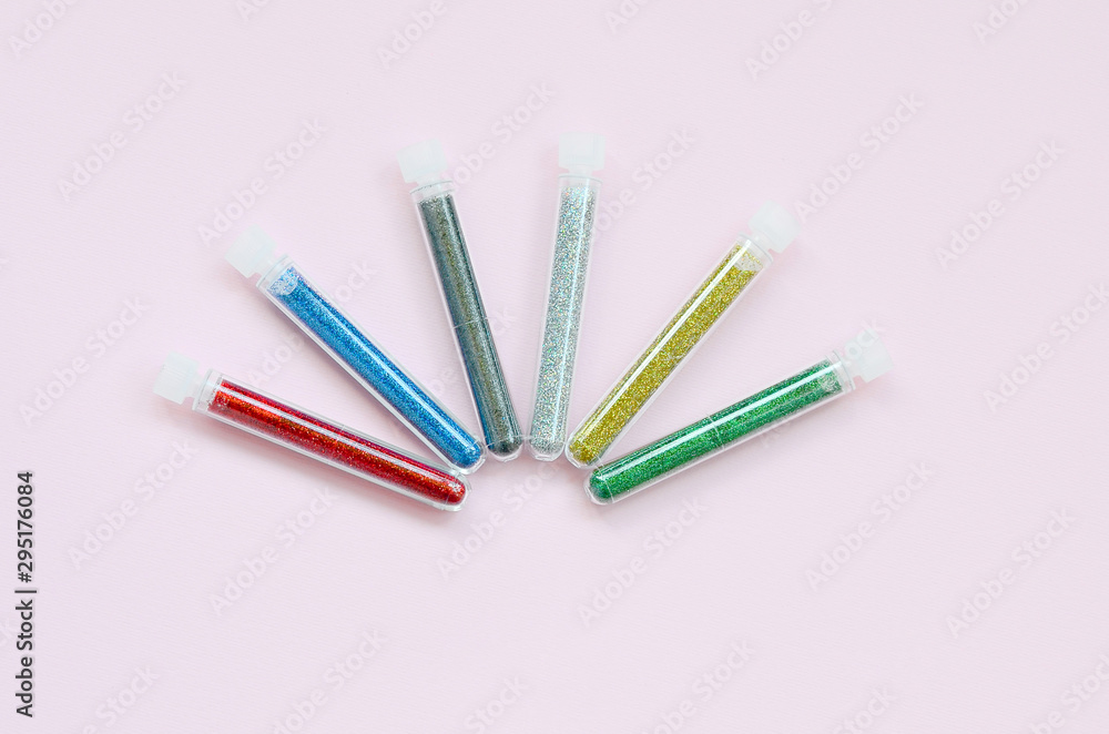 Colorful glitters lies on pastel pink background. Many long bottles with multi-colored bright sparkles for nail polish Colorful glitters lies on pastel pink background. Many long bottles with multi-colored bright sparkles for nail polish
