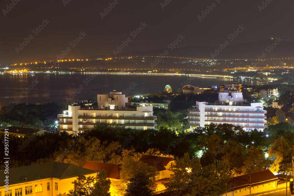 Night view of Glendzhik bay and beach including the hotels and buildings. Roofs of resident buildings and top of trees in foreground.
