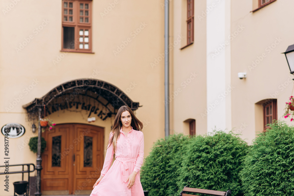 A young, beautiful girl in a pink dress walks around the city. Photo close - up and General plan. Girl sitting on a bench.