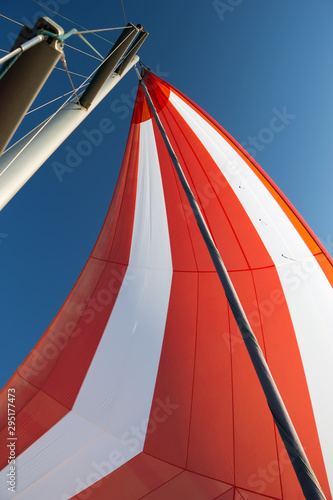 White-red developing sail on a yacht mast against the blue sky  bottom view. Traveling by sea on sunny day. Leisure activities at sea. Competitions on yachts. Beautiful background for bright postcard