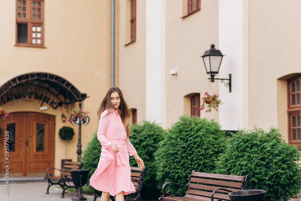 A young, beautiful girl in a pink dress walks around the city. Photo close - up and General plan. Girl sitting on a bench.