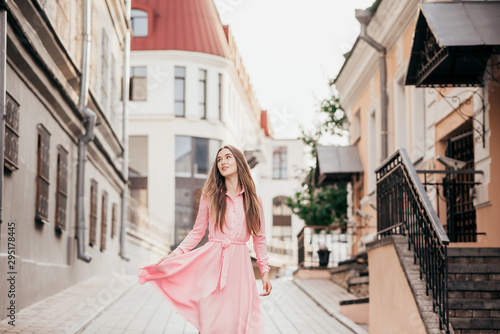 A young, beautiful girl in a pink dress walks through the beautiful streets in the city. Very beautiful portraits of a girl in the city.