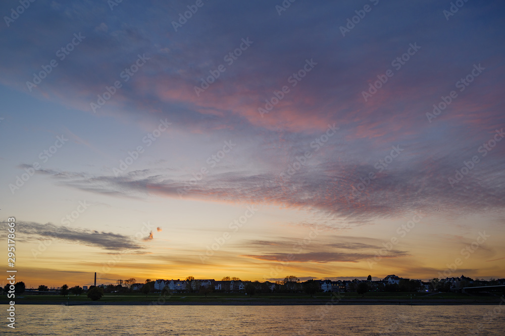 Silhouette view of city on riverside and Rhine River with beautiful dramatic purple, blue and golden sky during twilight sunset time.