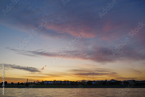 Silhouette view of city on riverside and Rhine River with beautiful dramatic purple, blue and golden sky during twilight sunset time.