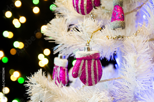 Christmas white tree with pink shiny toys highlighted in blue. Blurred dark background with multi-colored garland highlights. New Year s toys of pink and gray color. New Year 2020