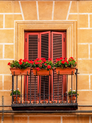 A juliet balcony with red louvre doors and small red flowers in window planters