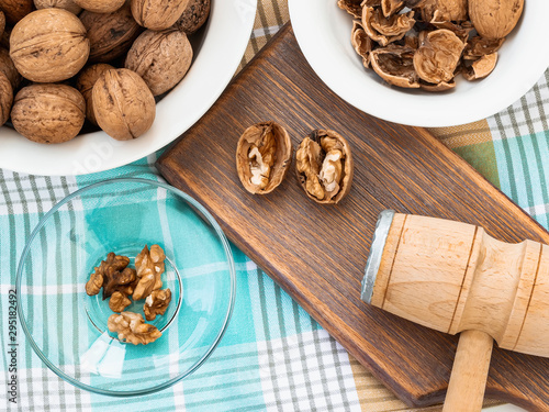 Whole walnuts, shells and kernels in a bowls around a brown wooden board with cracked nuts and wooden meat mallet. Natural unbleached Juglans regia.