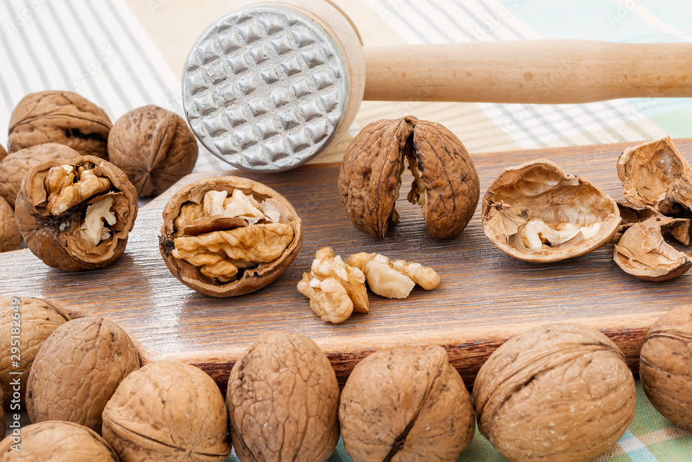 Front view of whole and cracked walnuts (Juglans regia) near wooden meat mallet on a brown wooden board. Natural unbleached nuts. Vegetarian. Front view of whole and cracked walnuts (Juglans regia) near wooden meat mallet on a brown wooden board. Natural unbleached nuts. Vegetarian.