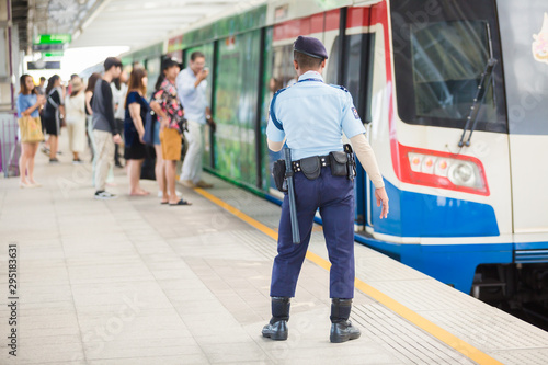 A security guard standing and watch to safety with blurry passengers going up and down from the BTS Skytrain.