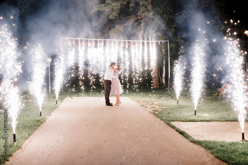 A crowd of young happy people during celebration. Sparkler in hands on a wedding - bride, groom and guests holding lights in hand. Sparkling lights of bengal fires. Wall of fountains.