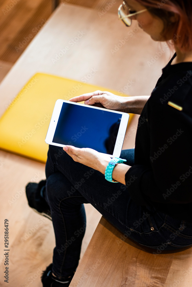 Obraz premium Portrait of a young student working on her digital tablet computer sitting in the auditorium. She wears jeans, glasses and a watch. Mobile and technology app.