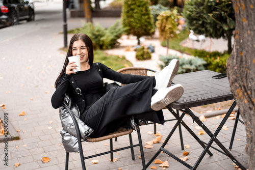 girl in black clothes and white sneakers drinking coffee and talking on the phone
