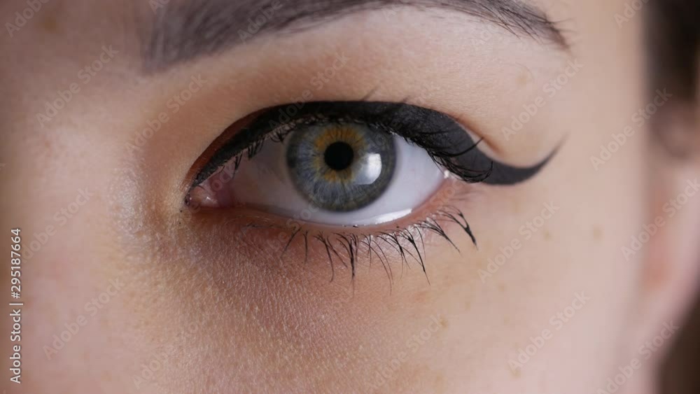Eye iris contracting, pupil dilation, woman blue eye looking to camera in macro close-up Eye iris contracting, pupil dilation, woman blue eye looking to camera in macro close-up