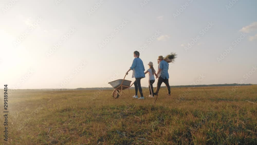 Young family having fun outdoors in their farm. Gardener woman pushing wheelbarrow with vegetables at sunset. Family working at the countryside. Silhouette workers go at sunset. Happy family concept. Young family having fun outdoors in their farm. Gardener woman pushing wheelbarrow with vegetables at sunset. Family working at the countryside. Silhouette workers go at sunset. Happy family concept.