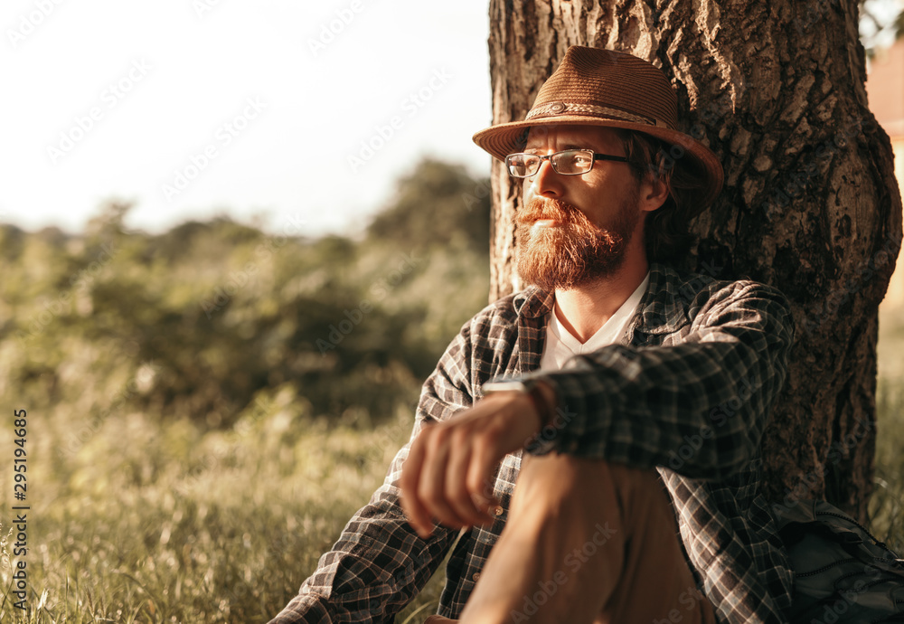 Thoughtful traveler resting near tree Thoughtful traveler resting near tree