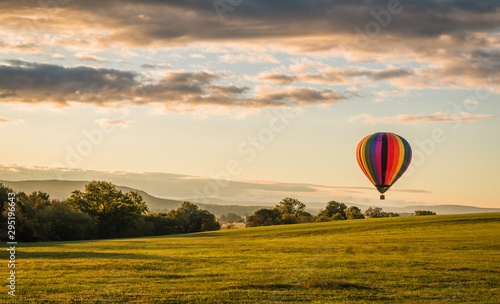 Photography Rainbow hot-air balloon floats over valley at sunrise