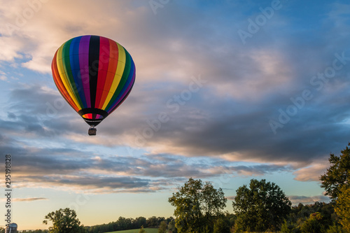 Rainbow hot-air balloon floats over grassy field and trees at sunrise © rabbitti