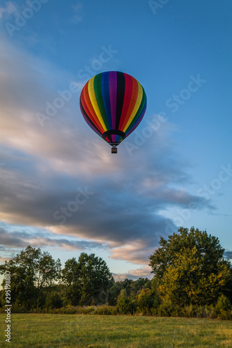 Rainbow hot-air balloon floats over grassy field and trees at sunrise © rabbitti