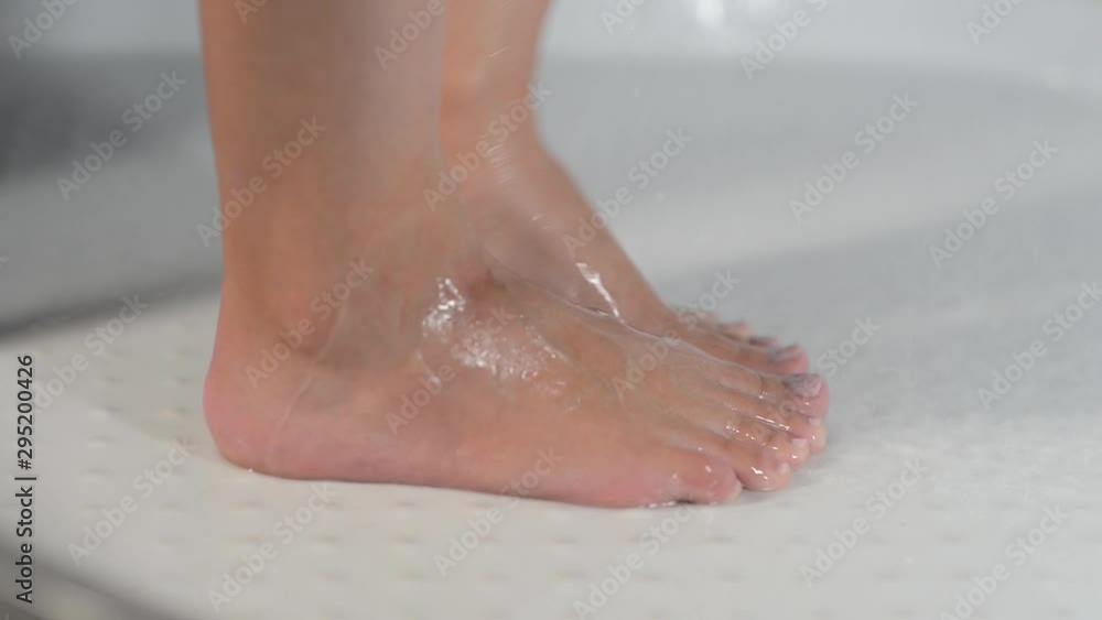 a woman is standing in the shower and washes herself with a shower gel. Close-up of legs a woman is standing in the shower and washes herself with a shower gel. Close-up of legs