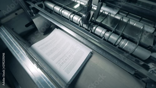 Paper pages with text are getting mechanically issued. Printing factory equipment.