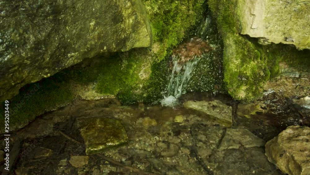 Natural spring water flowing through crack in rocks into small rocky pool
