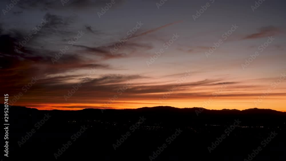 Time Lapse-Sky darkens with an orange glow and City lights appear as night comes over desert hills Time Lapse-Sky darkens with an orange glow and City lights appear as night comes over desert hills