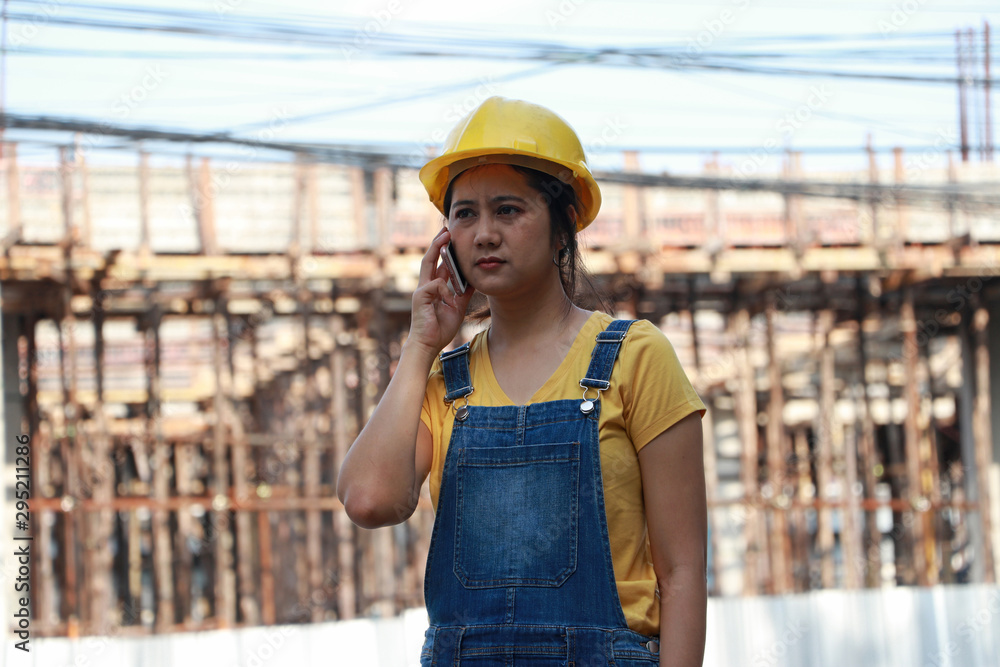 Female civil engineer or architect with yellow helmet, standing and calling with mobile phone. Female civil engineer or architect with yellow helmet, standing and calling with mobile phone.