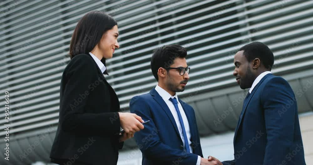 Caucasian beautiful young woman in business style and Arabian handsome businessman meeting and shaking hands with African American male colleague. Outdoors. Caucasian beautiful young woman in business style and Arabian handsome businessman meeting and shaking hands with African American male colleague. Outdoors.
