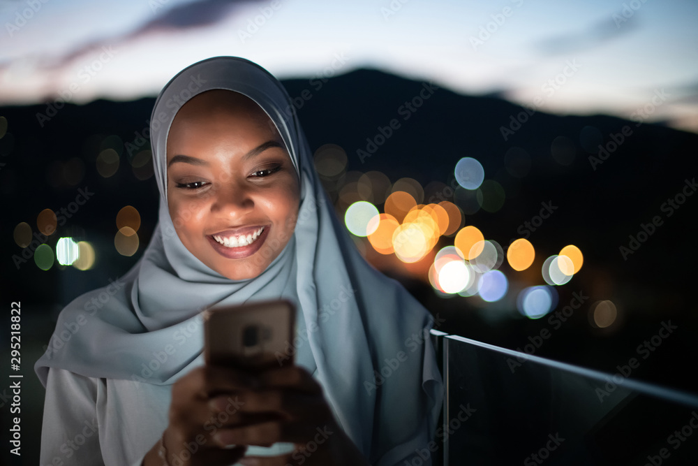 Young Muslim woman on  street at night using phone - obrazy, fototapety, plakaty 