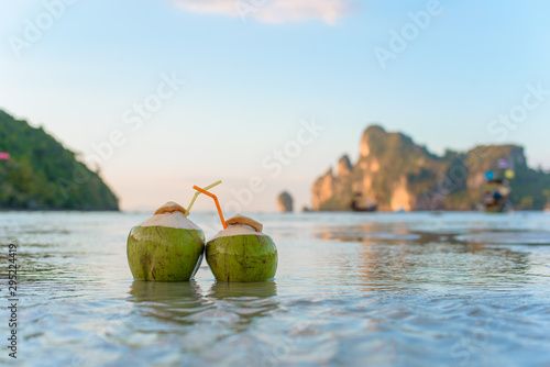 Two drinking coconut with straws on a tropical beach.