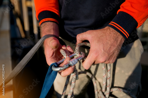 Rope access worker inspecting closing rigging on locking Karabiner its attached into safety 25 tone sling and bunny ears knot prior to used on structure beam roof top high rise building site, 