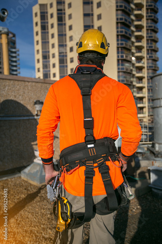 Picture showed the back side of male rope access worker dressing with industry fall protection yellow helmet abseiling safety body harness prior to work on construction site Sydney CBD, Australia  